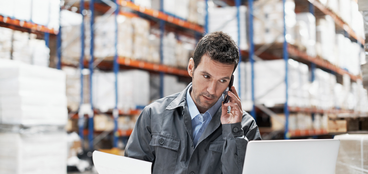 man on the phone and in front of laptop in a warehouse