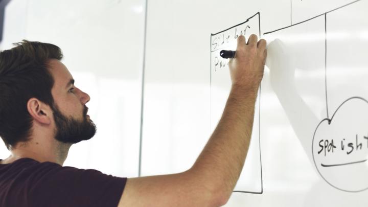 Man with a beard writing on a white board