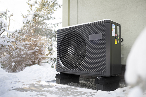 air source heat pump unit standing against the residential building wall. Shot in winter, in a snowy setting