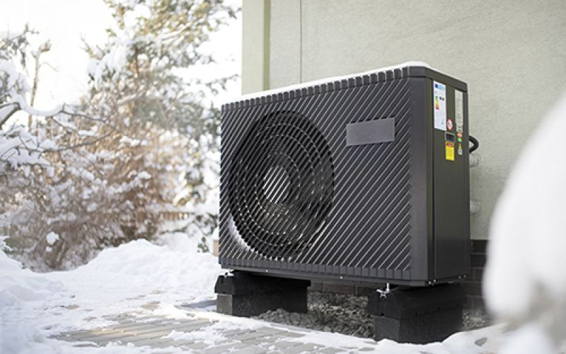 air source heat pump unit standing against the residential building wall. Shot in winter, in a snowy setting