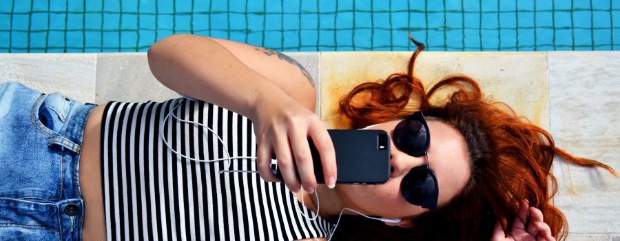 Young woman next to swimming pool, checking her phone