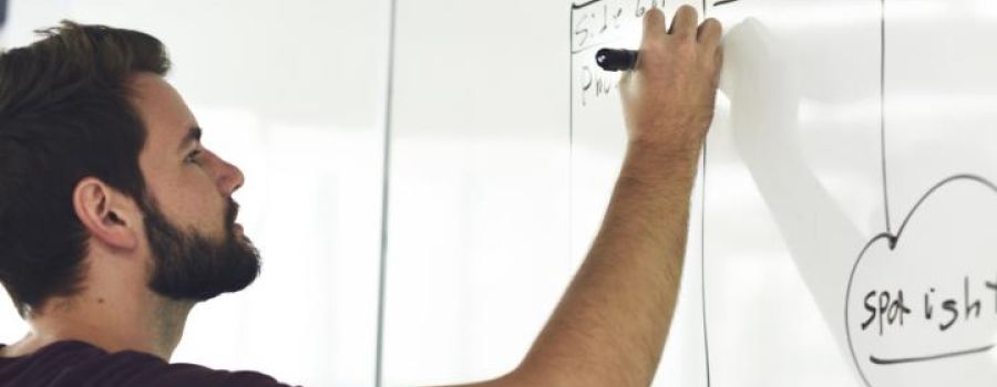 Man with a beard writing on a white board