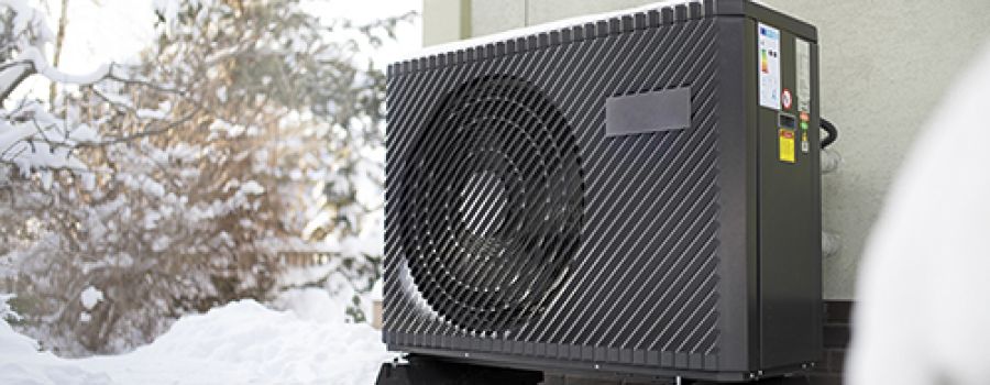 air source heat pump unit standing against the residential building wall. Shot in winter, in a snowy setting